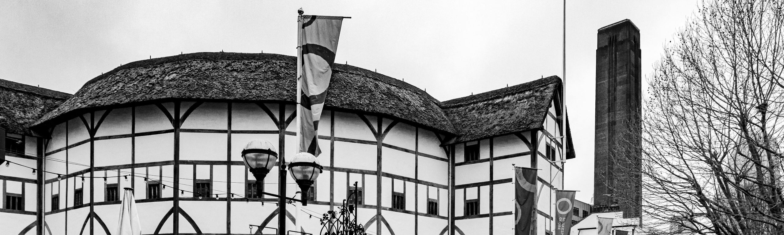 A black and white photo shows the outside of the Globe Theatre in London, with a thatched roof and curving timber framed walls.