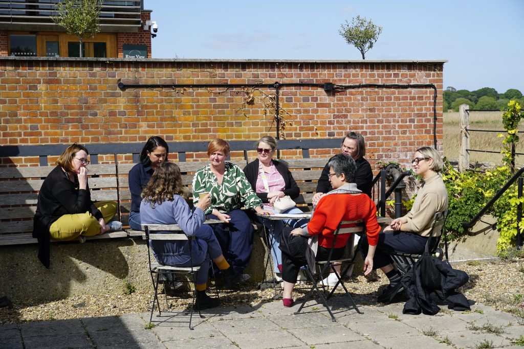 A group of delegates sit outside on a sunny patio, the photo captures them mid-discussion. 