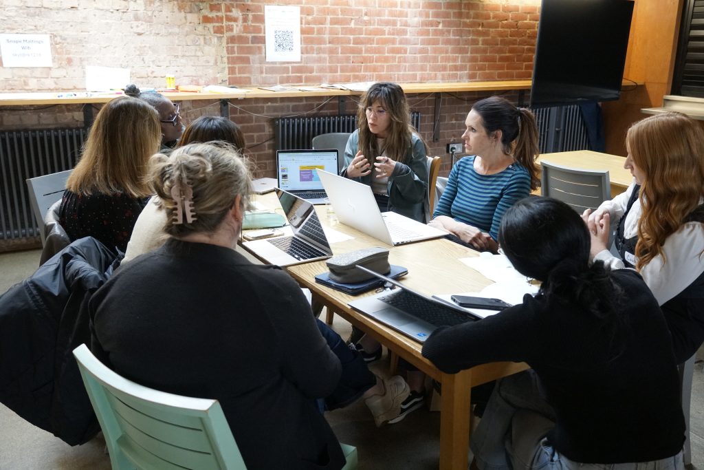 A group of delegates sit at a table together, one person is giving a presentation with their laptop.