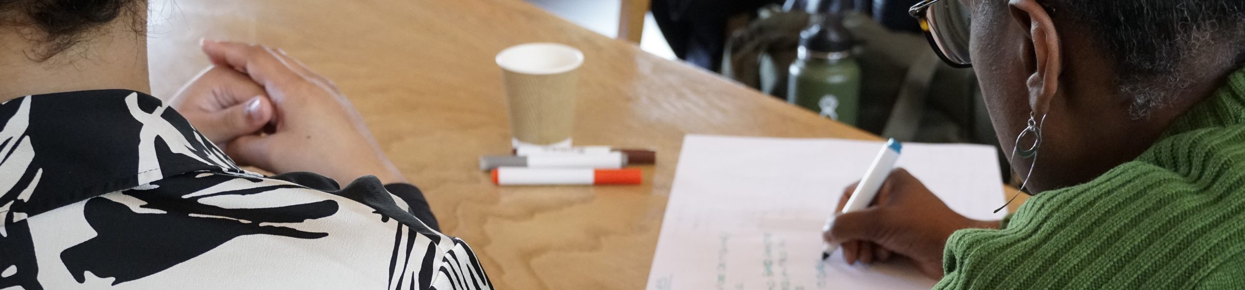 A photo shows two people at a table, one is writing notes on paper.