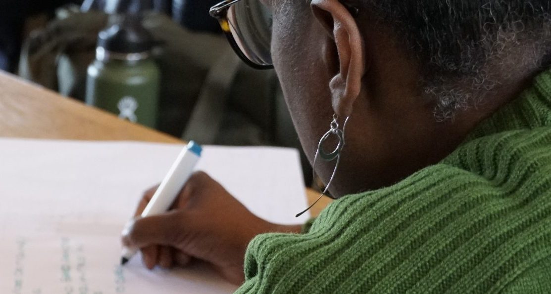 A photo shows someone writing on paper at a table.