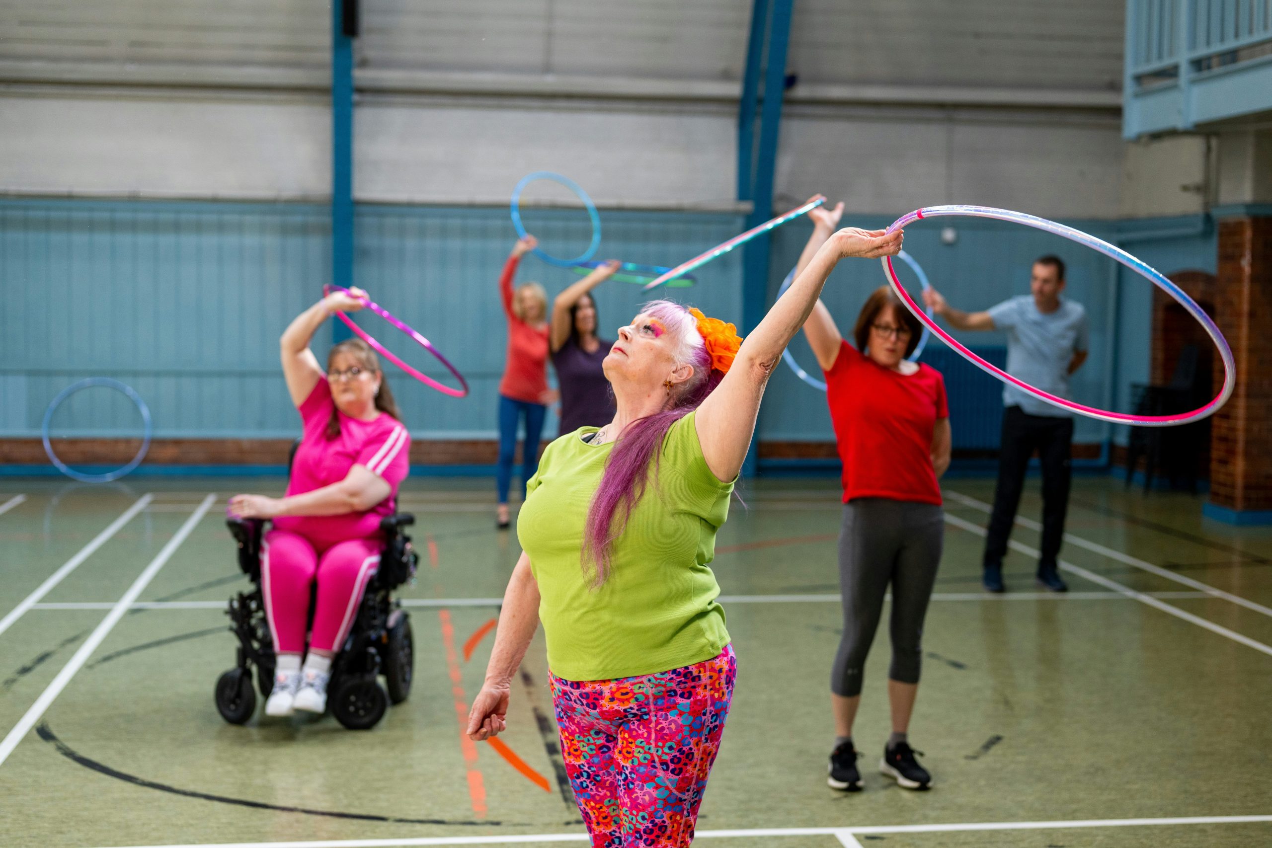 A group of people dance with hoops in a sports hall.