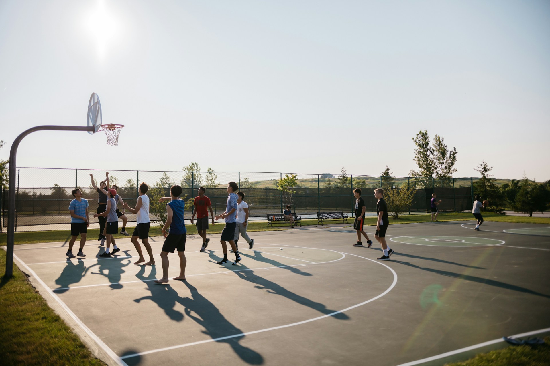 A photo shows a group of boys playing basketball outside on a sunny day.